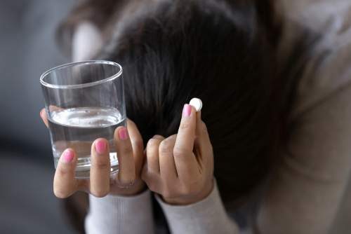 Woman with a headache holding a pill and a glass of water