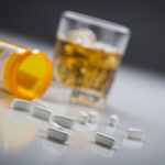 white-tablet-pills-spilling-out-of-prescription-bottle-with-glass-of-alcohol-on-table